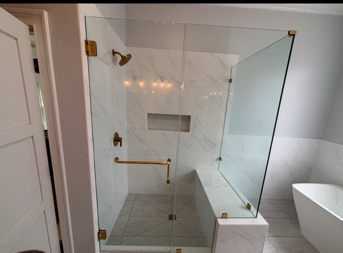 Frameless glass shower with gold fixtures and freestanding soaking tub